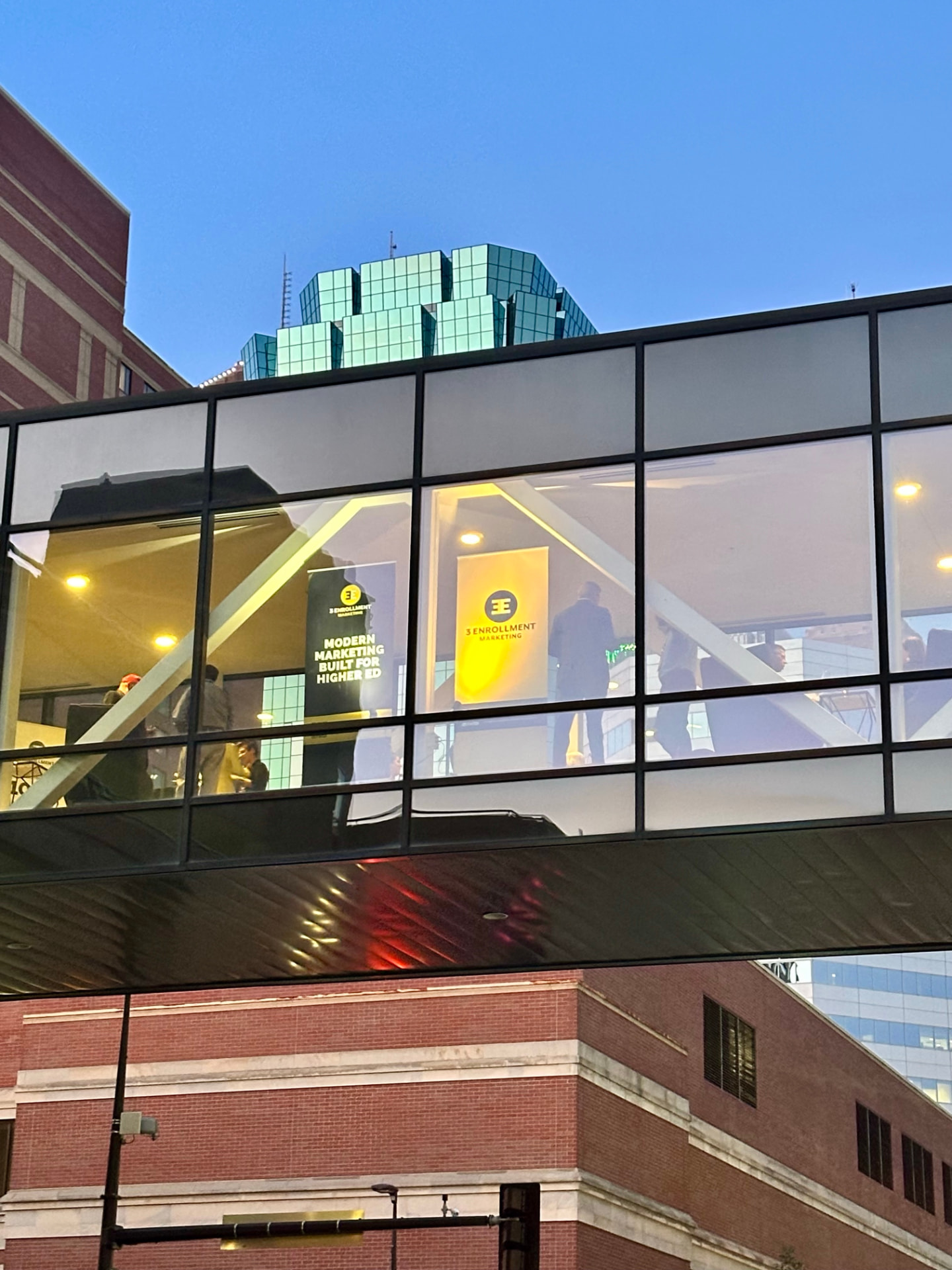 The glass Hotel Ivy skyway seen from the street below, with 3E Enrollment Marketing banners hanging inside