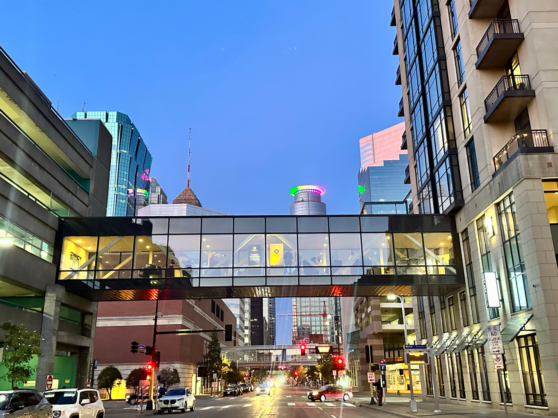 The Hotel Ivy skyway glowing above a downtown Minneapolis street at dusk, with 3E banners visible through the glass
