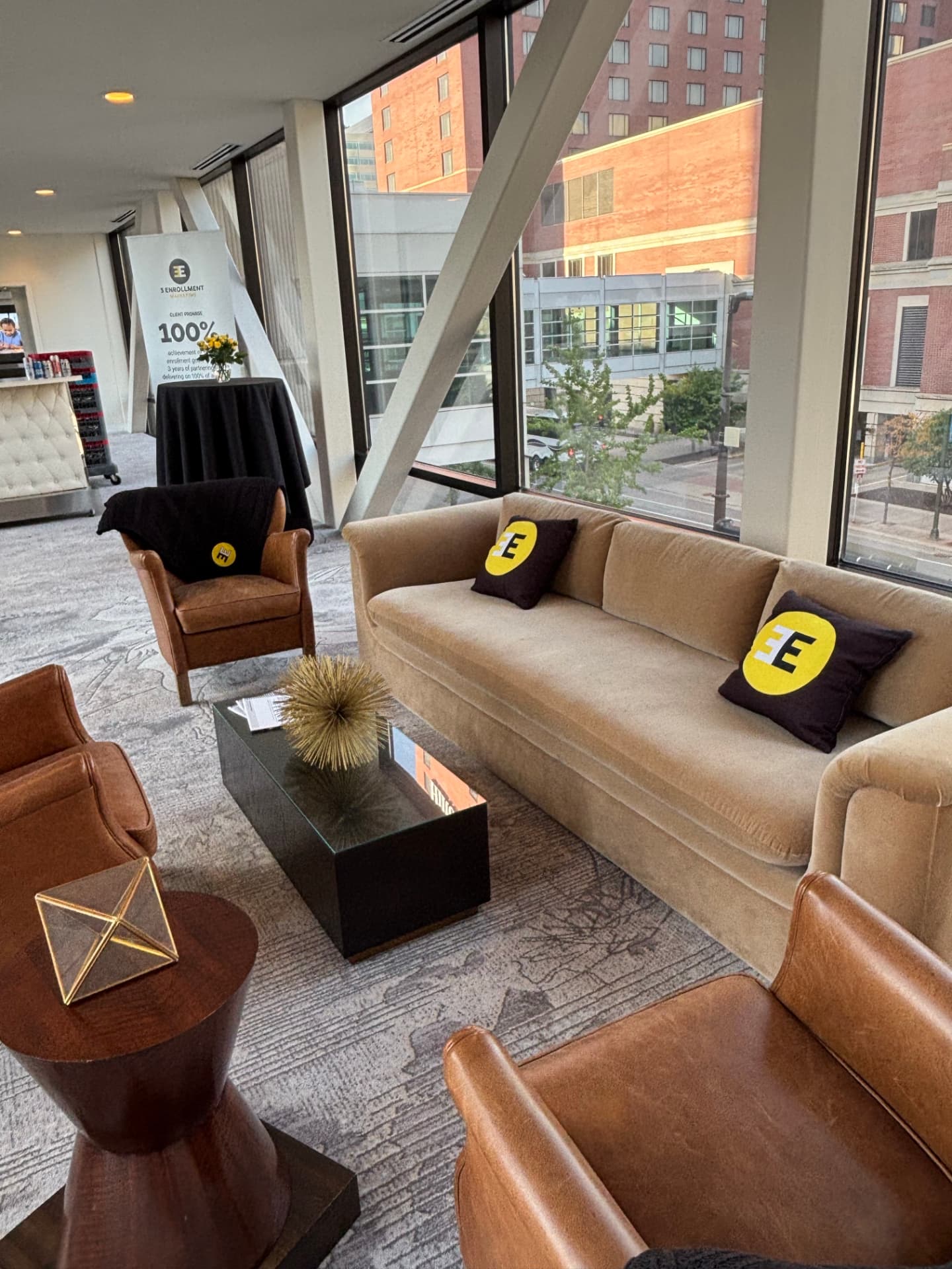 The Hotel Ivy skyway lounge set with a beige sofa, leather armchairs, and yellow 3E throw pillows
